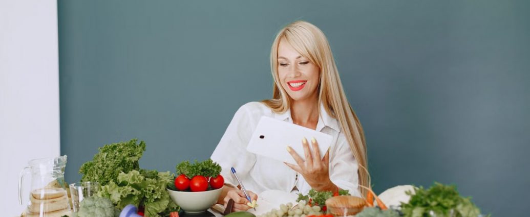Woman using a tablet surrounded by fresh vegetables at a table, showcasing healthy lifestyle and technology.