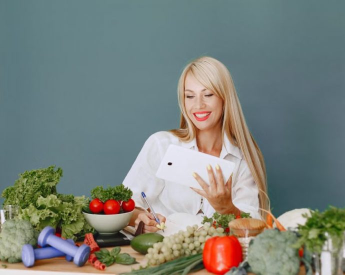 Woman using a tablet surrounded by fresh vegetables at a table, showcasing healthy lifestyle and technology.