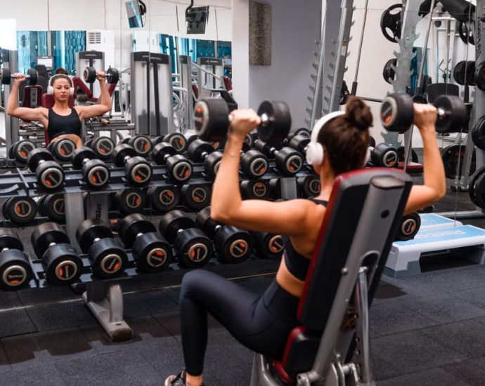 Woman exercising in the gym lifting dumbbells with headphones on for a strength-building workout.